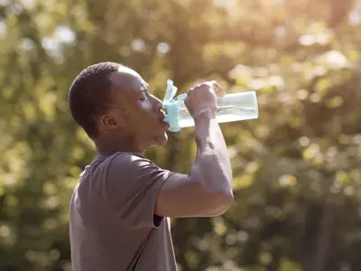 Man drinking from large water bottle outdoors in the summer.