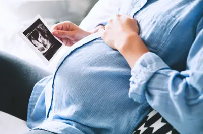 Close up of a mother's pregnant stomach as she holds an ultrasound image.