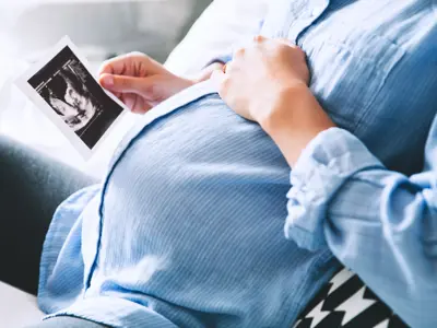 Close up of a mother's pregnant stomach as she holds an ultrasound image.