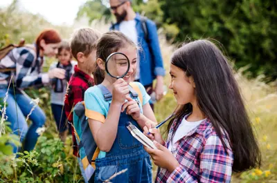 Children outdoor at a summer camp on a geo caching hunt holding a magnifying glass and clip board