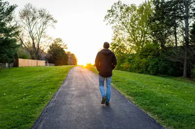 Silhouette of man walking towards sunset along paved path in spring.