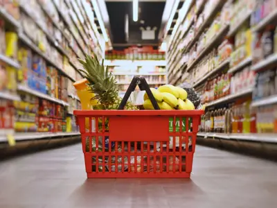 Red basket of groceries sitting on the floor in the middle of an isle at a grocery store.