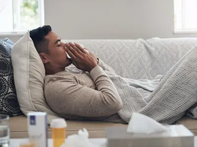 Man laying on couch sneezing into tissue