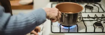 Person holding a pot of boiling water on a stove