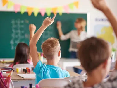 Students in classroom raising their hands to answer a question.