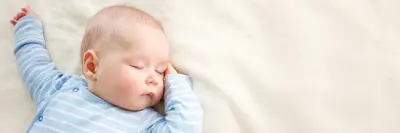 Baby in blue jumper sleeping on a white blanket.