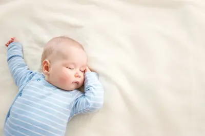 Baby in blue jumper sleeping on a white blanket.