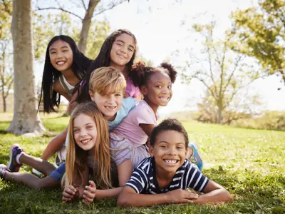 Multi-ethnic group of kids lying on each other in a park.