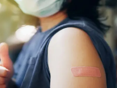 A masked person giving thumbs up with band-aid on arm